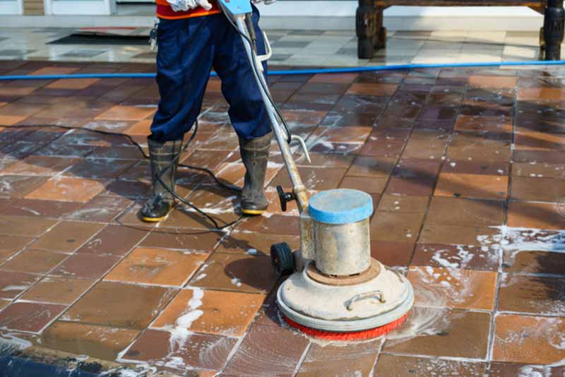 worker in protective workwear cleaning floor titles with a a large hand held machine