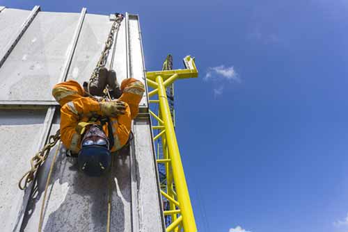 man wearing orange high visibilty workwear suspended from ropes working at extreme heights