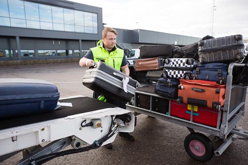 baggage handler in a fluorescent vest moving bags from an aeroplane on a trailer 