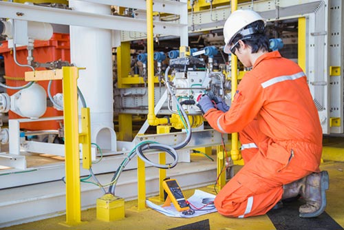 Industrial electrician working on a piece of machinery wearing a orange high visibility coverall