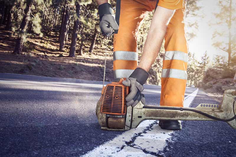 worker in high visibility workwear pulling over a brushcutter